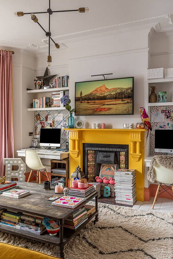 an eclectic living room with open shelves, a desk, a neutral chair, a fireplace with a yellow mantel, some books and some decor