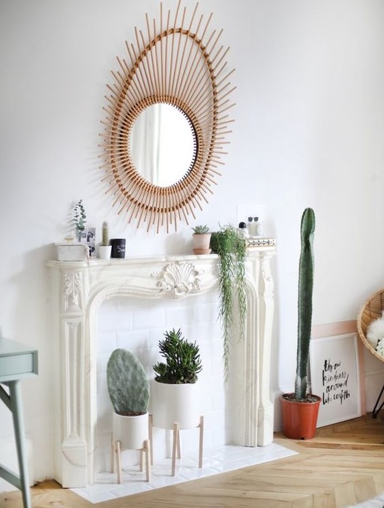 an elegant faux fireplace with potted plants and cacti on display, with a chic and beautiful mirror and some bottles