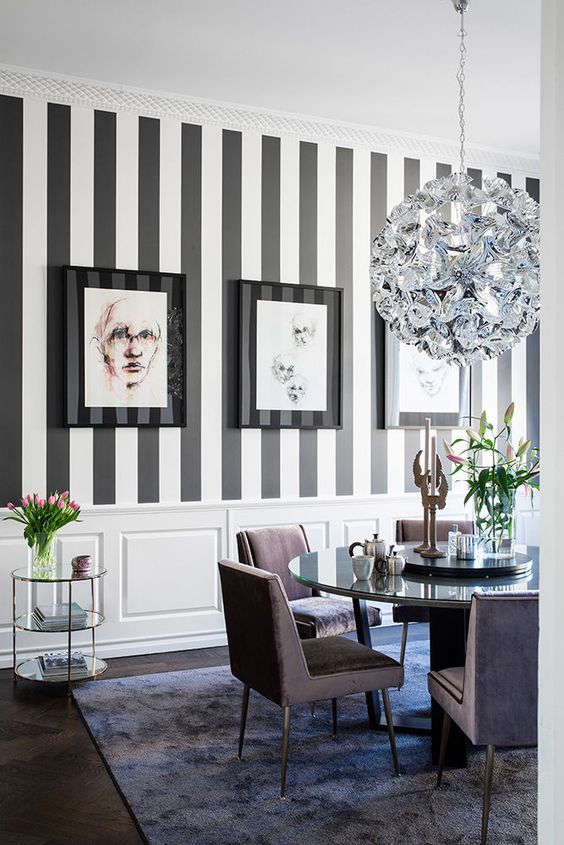 an exquisite dining room with a striped black and white wall, a chic shiny chandelier, lavender chairs and a mirror table