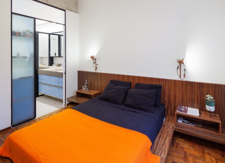 The master bedroom shows off darker wooden furniture and parquet floors, sliding doors lead to a grey and blue bathroom The master bedroom shows off darker wooden furniture and parquet floors, sliding doors lead to a grey and blue bathroom