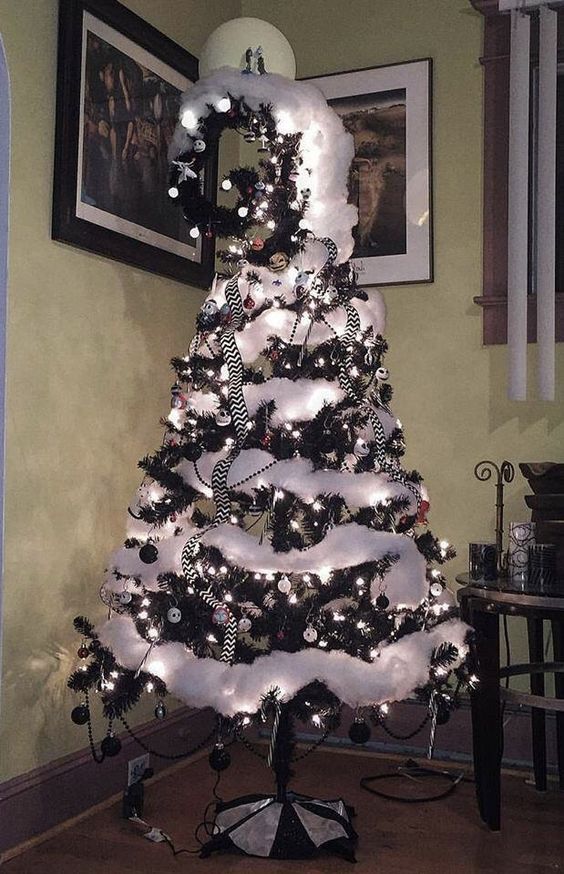 a black Christmas tree with black and white ornaments, white cotton snow, a swirled top and striped ribbons