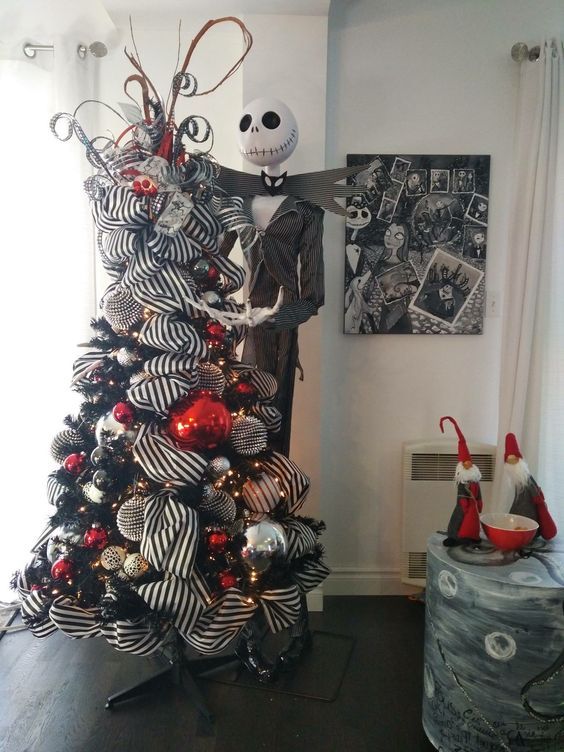a black Christmas tree with striped ribbons, gold, silver, red and black ornaments and a Jack Skellington figure next to it