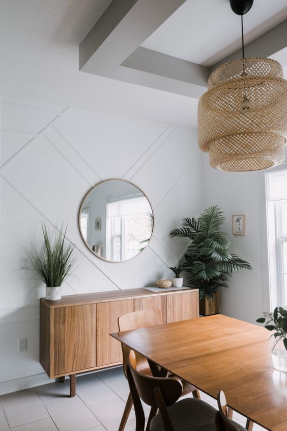 a chic mid-century modern dining room with a white paneled wall, elegant wooden furniture, a wicker pendant lamp and greenery