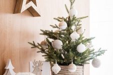 a chic tabletop Christmas tree with lights, tan and white oversized ornaments plus wooden decor around for a Nordic feel in the space