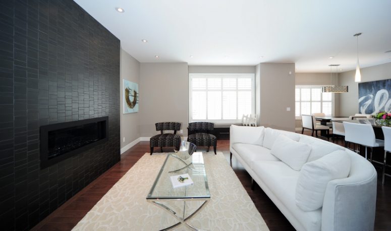 a contemporary living room with a black tile fireplace wall, a large curved sofa in white and elegant furniture around