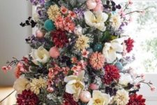 a flocked Christmas tree decorated with blooms and blooming branches, with blush ornaments and some dark foliage looks lovely