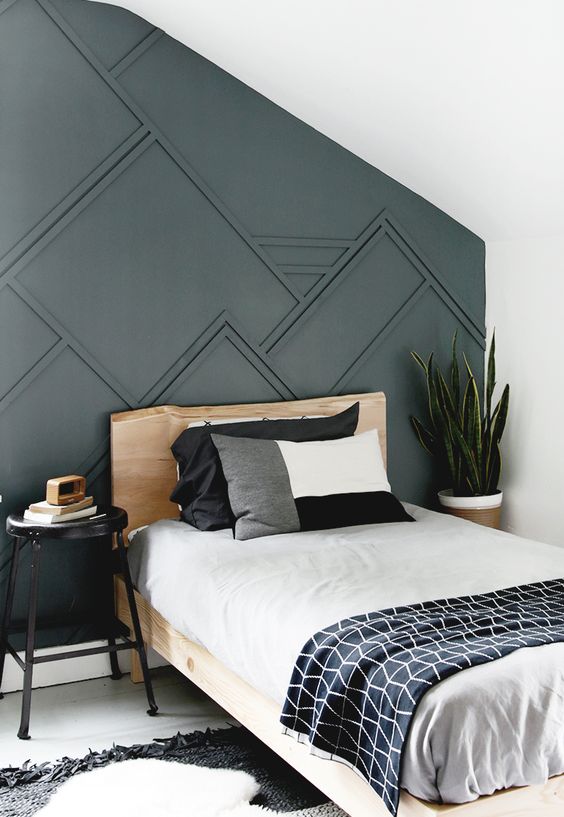 a guest bedroom with a graphite grey paneled wall, a wooden bed, graphic bedding and a statement plant in the corner