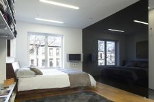 a minimalist monochromatic bedroom with a glossy black wall that brings drama and may hide a bathroom