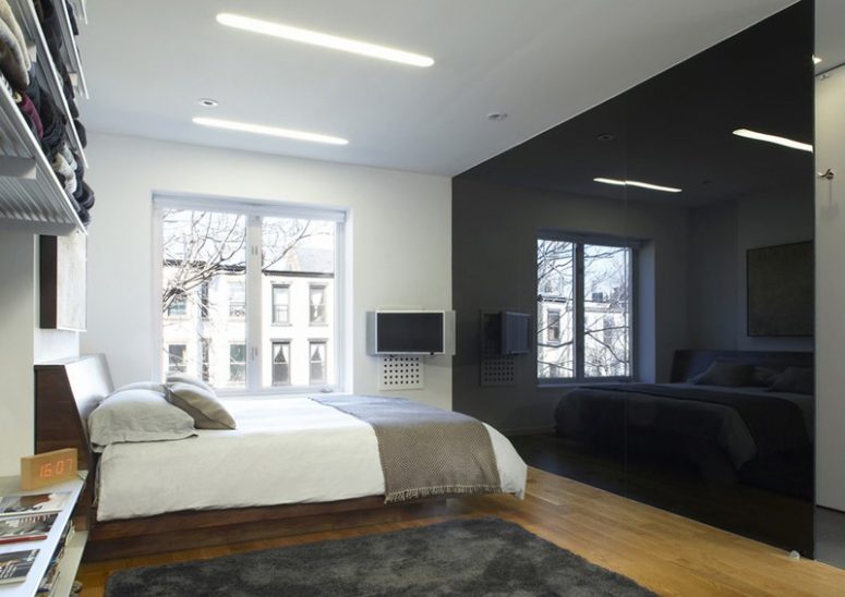 a minimalist monochromatic bedroom with a glossy black wall that brings drama and may hide a bathroom
