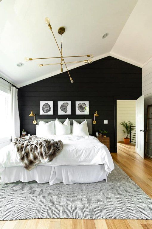 a modern farmhouse bedroom with a black wooden plank wall that makes a statement and touches of gold and brass for a shiny look