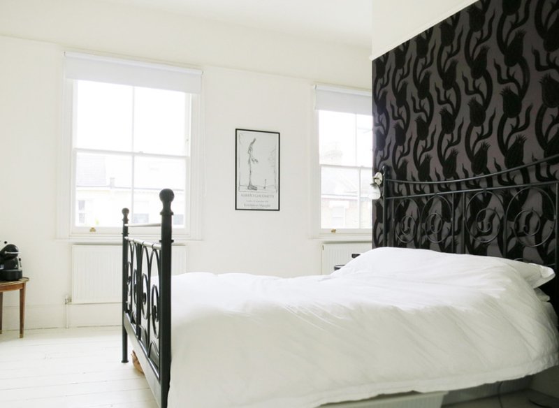 a monochromatic vintage inspired bedroom with a black floral wallpaper wall, a black forged bed and a chic artwork