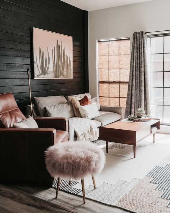 a neutral and warm-colored living room with a black plank wall, neutral furniture, pink and terracotta textiles and upholstery