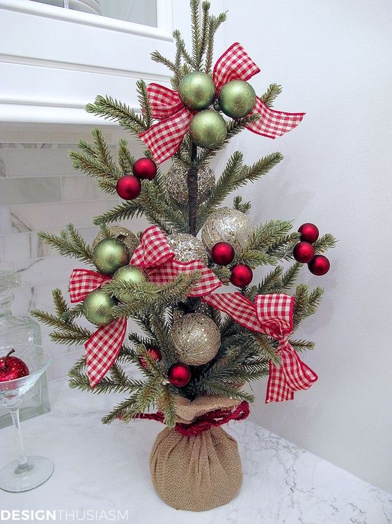 a pretty tabletop Christmas tree with green, red and shiny metallic ornaments and plaid bows plus a burlap sack for a rustic feel