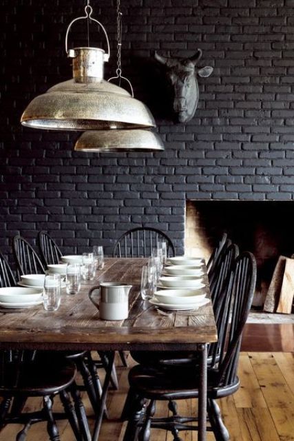 a vintage meets rustic dining room with a black brick wall, a wooden table and dark vintage chairs is very cozy