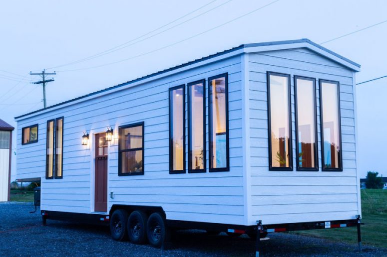This tiny home on wheels is a very simple and clean house, with white facades and a metal roof plus lots of windows