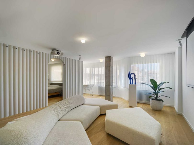 The living room got a large geometric sectional sofa with an ottoman, some plants and a sculpture plus a cocnrete pillar