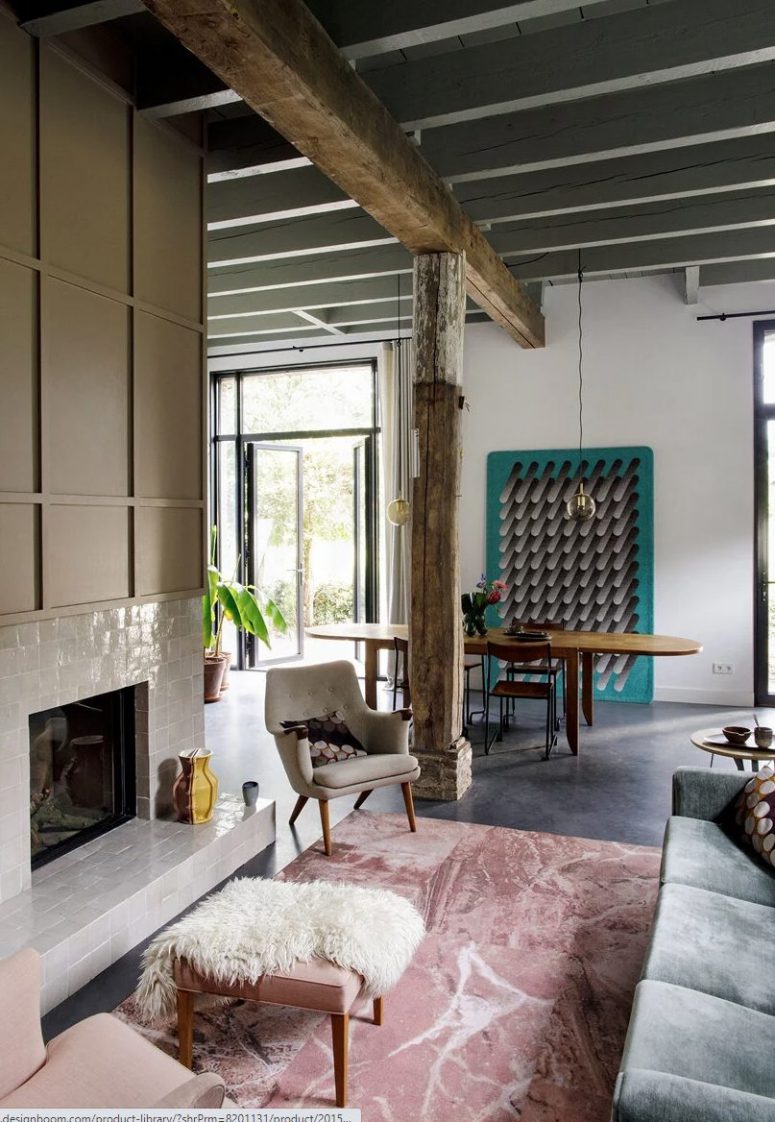The living room is done with a fireplace clad with white tiles, a grey sofa, wooden beams and pillars, a dining space with an oval table is adjoined here