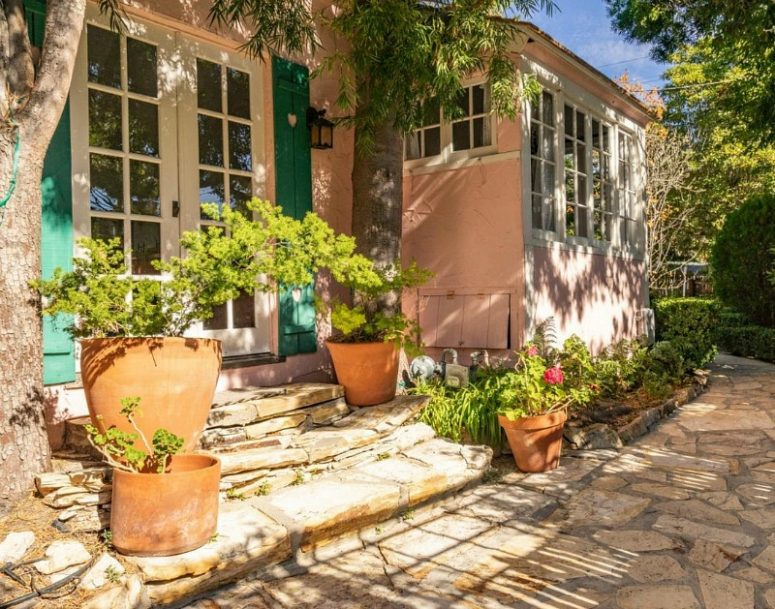 The house is surrounded by potted plants and blooms