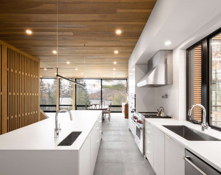 a modern kitchen with a stylish wooden ceiling The kitchen is done with sleek white cabinets, a wooden ceiling and a concrete floor plus a wooden space divider