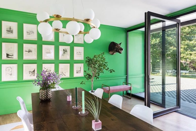 The dining room is done with a bold green wall, a pretty gallery wall, a wooden table and a pink bench