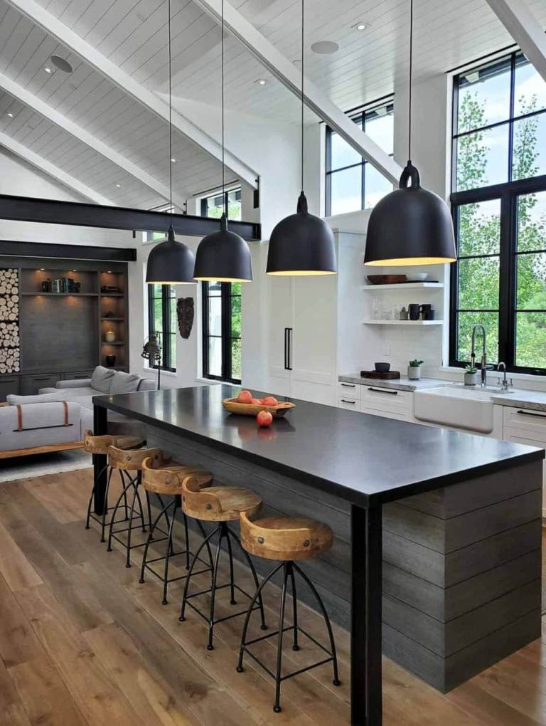 The kitchen is done with white cabinetry, with a dark kitchen island, pendant lamps and wooden stools