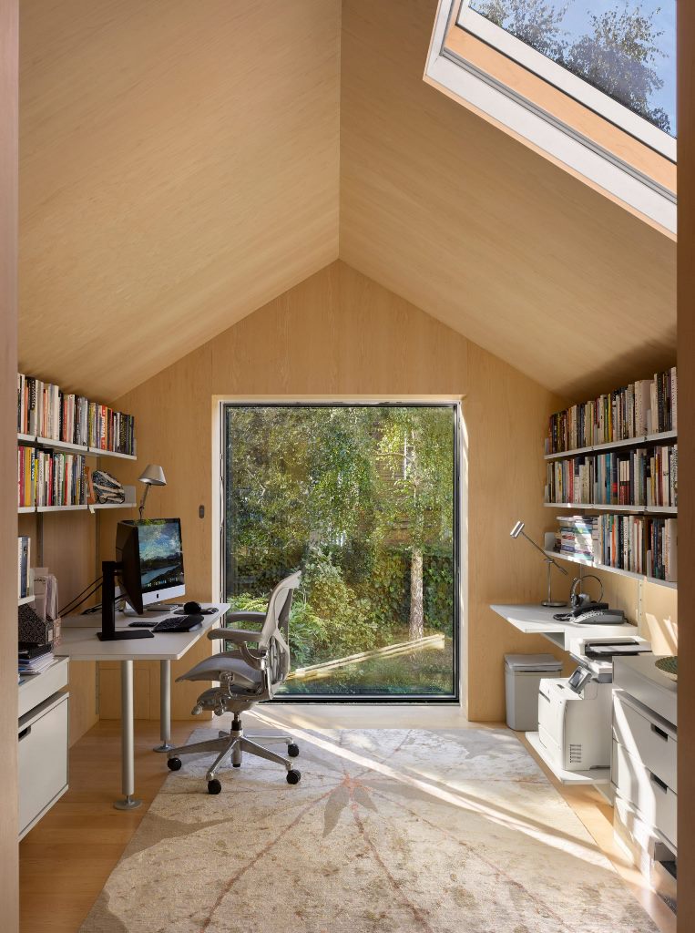 There's a home office with a large window and a skylight, with comfy furniture and open shelves