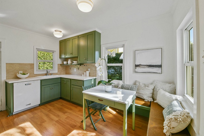 The kitchen is done with green cabinets and a table, with a corner seating and lots of pillows
