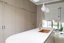 06 The kitchen is done with tan sleek cabinets that are built-in and are fully closed, while a large curved kitchen island makes a statement with its terrazzo part