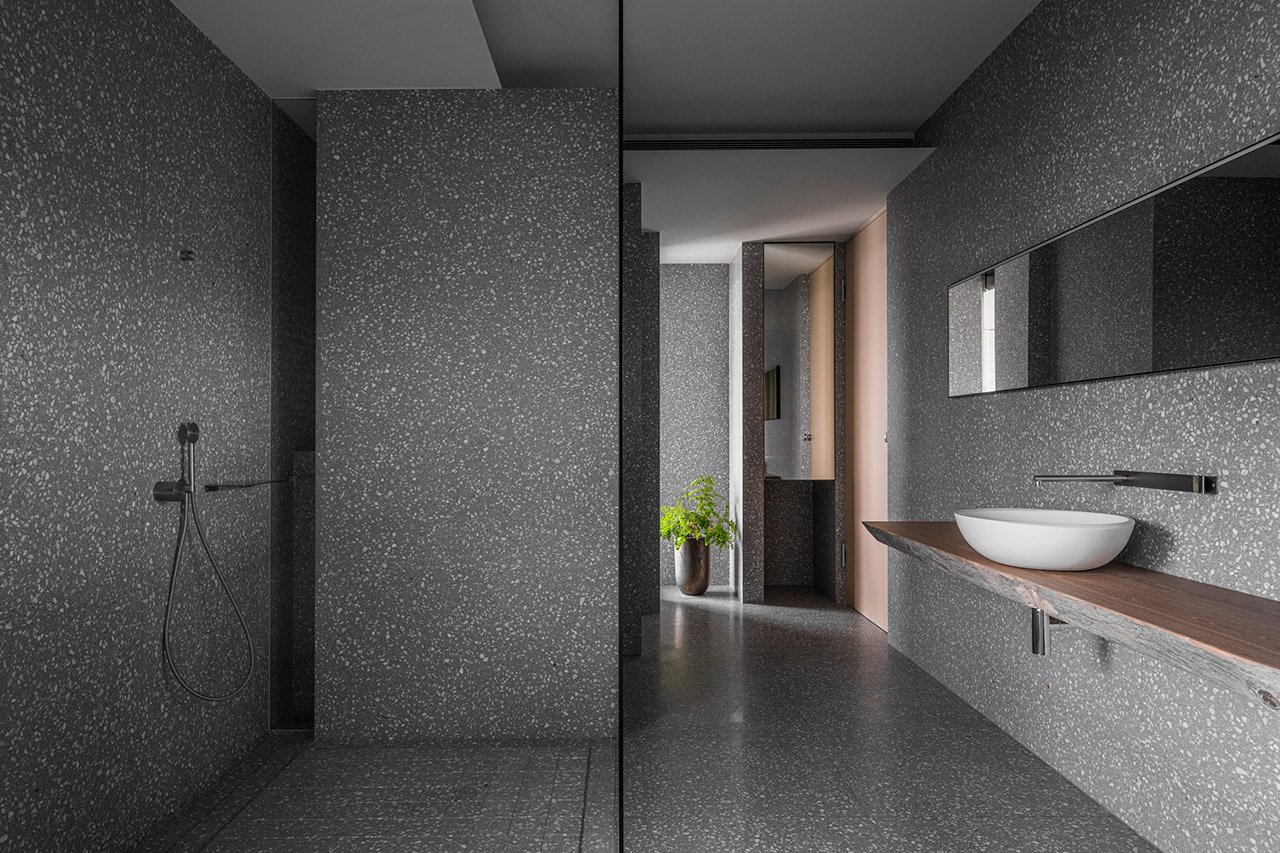 The bathroom is clad with grey terrazzo and features some wood to soften it