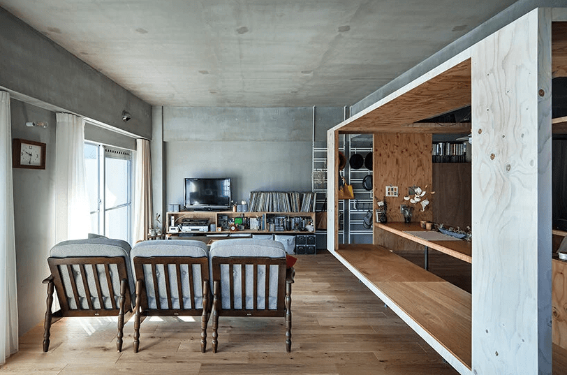There's a living room with some chairs, a sofa, a TV and a TV unit with books and other stuff