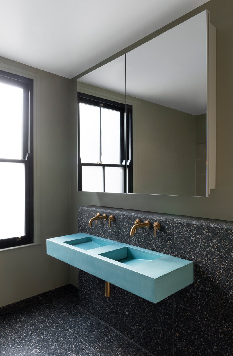 The bathroom is done wiht dark terrazzo tiles, a blue double sink