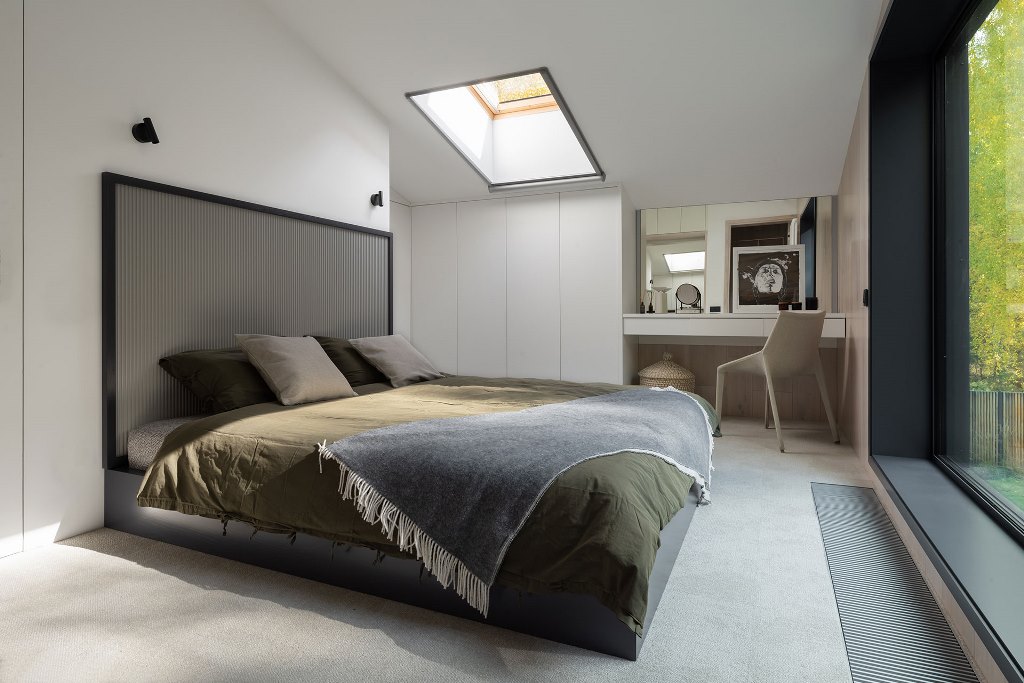 The bedroom shows off a large and comfy bed, a cozy nook and sleek storage, a skylight and cool artworks