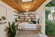 09 The guest cottage features a modern boho bedroom with floating shelves, some potted plants and a wooden ceiling