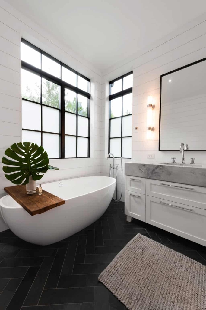 An oval soaking tub is placed at the far end of the bathroom, where it’s framed by both windows