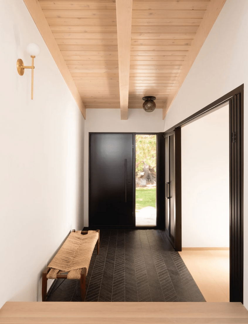 The entryway is simple and modern, clad with dark tiles and with a woven bench