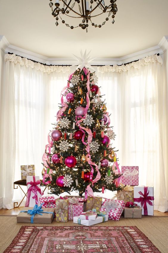 a bold Christmas tree decorated with pink and pink sequin ornaments, pink ribbons, lights and large snowflakes and a large star on top