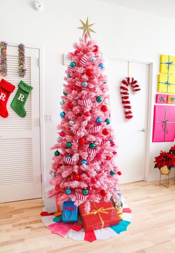 a hot pink Christmas tree decorated with super colorful ornaments and striped ribbons, topped with a gold star and with gifts
