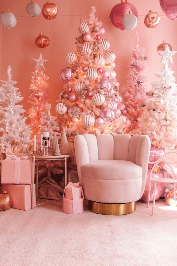 a pink Christmas space with a whole bunch of pink trees with ornaments, a blush chair and some pink gift boxes
