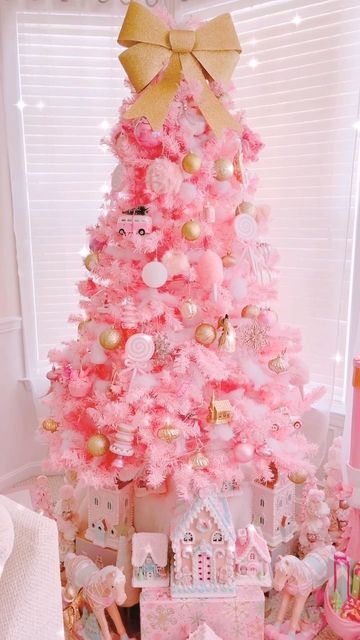 a pink Christmas tree with white and gold ornaments and some whimsical decorations plus a gold bow on top