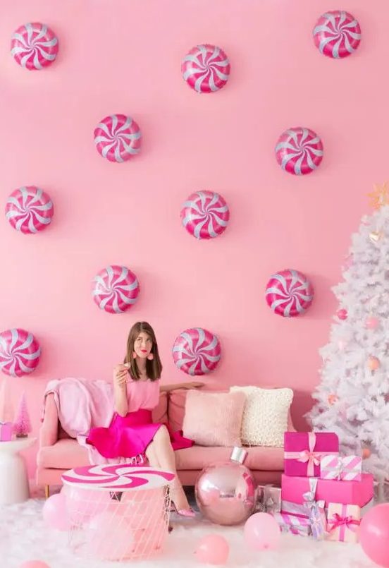 a pink holiday space with peppermints on the wall, pink furniture and balloon and pink ornaments on a white Christmas tree