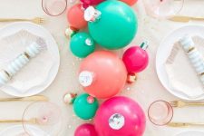bold and fun holiday tablescape with green, pink and fuchsia ornaments as a centerpiece, pink glasses, gold cutlery and printed plates