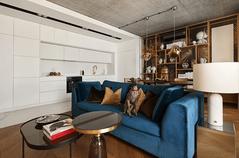 The kitchen is sleek and all-white, it seems to be built in on onsde of the open layout