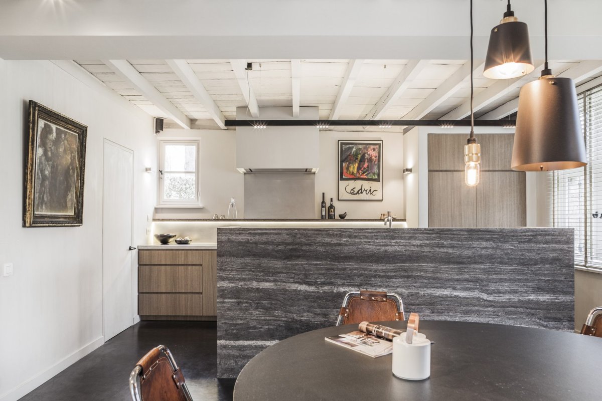 The kitchen is done with grey cabinetry, a stone kitchen island, pendant lamps, the dining space is here