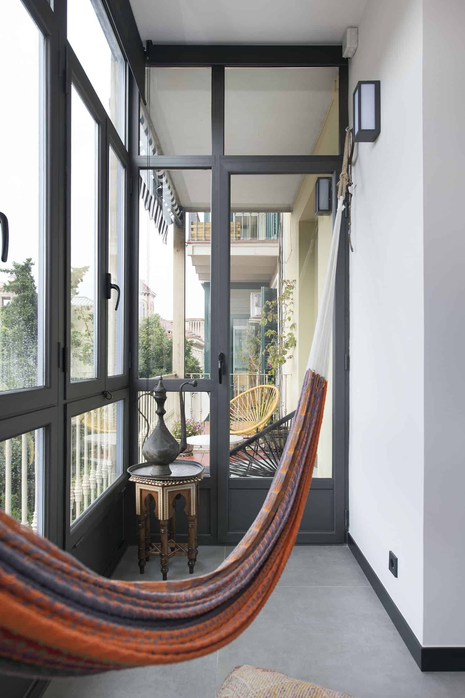 The balcony is glazed and is decorated in boho style, with a boho hammock, a boho table, a tray and a teapot