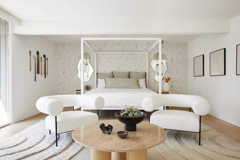 The bedroom is neutral, with a wallpaper wall, white furniture, a wooden table and a gallery wall