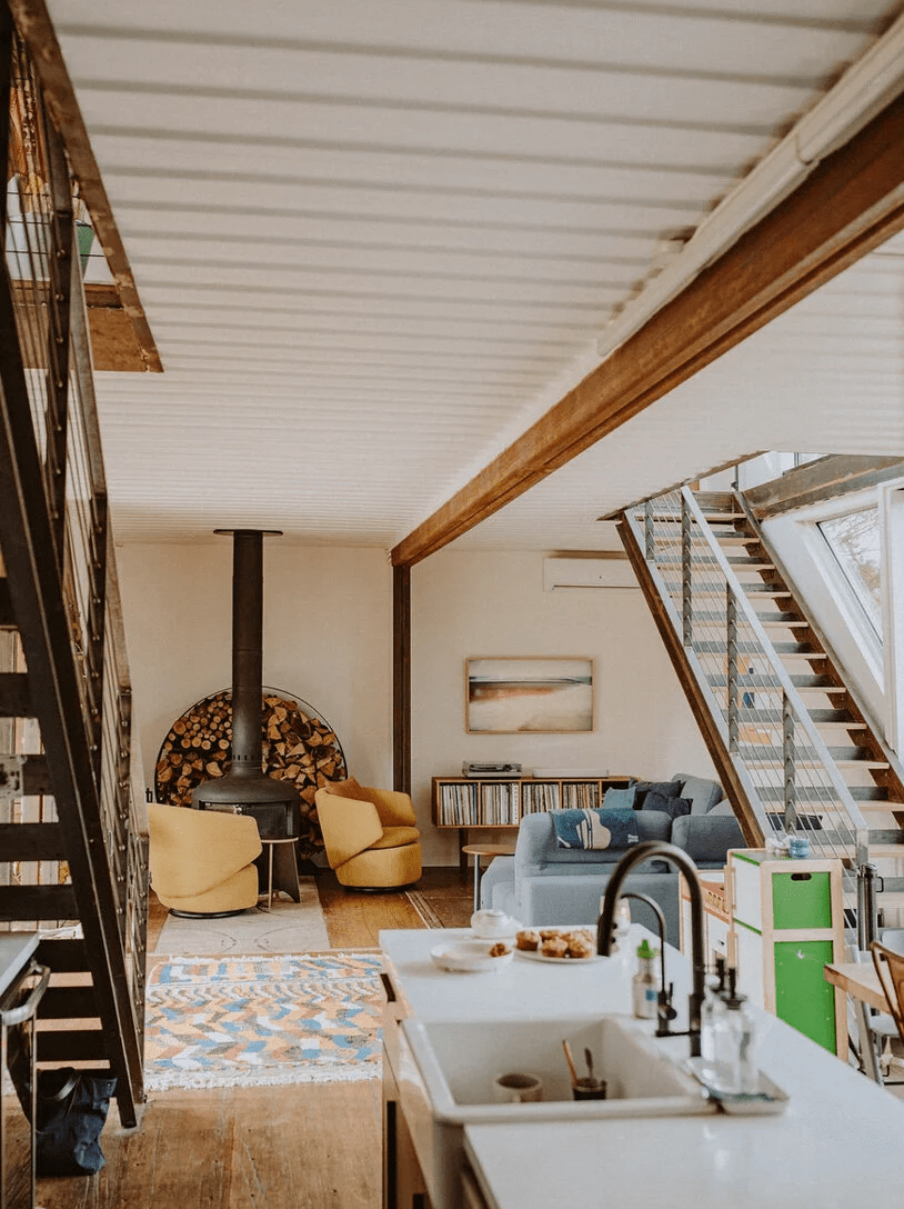 The living room shows off some honey yellow chairs, a hearth, a blue sofa and elegant mid-century modern shelves