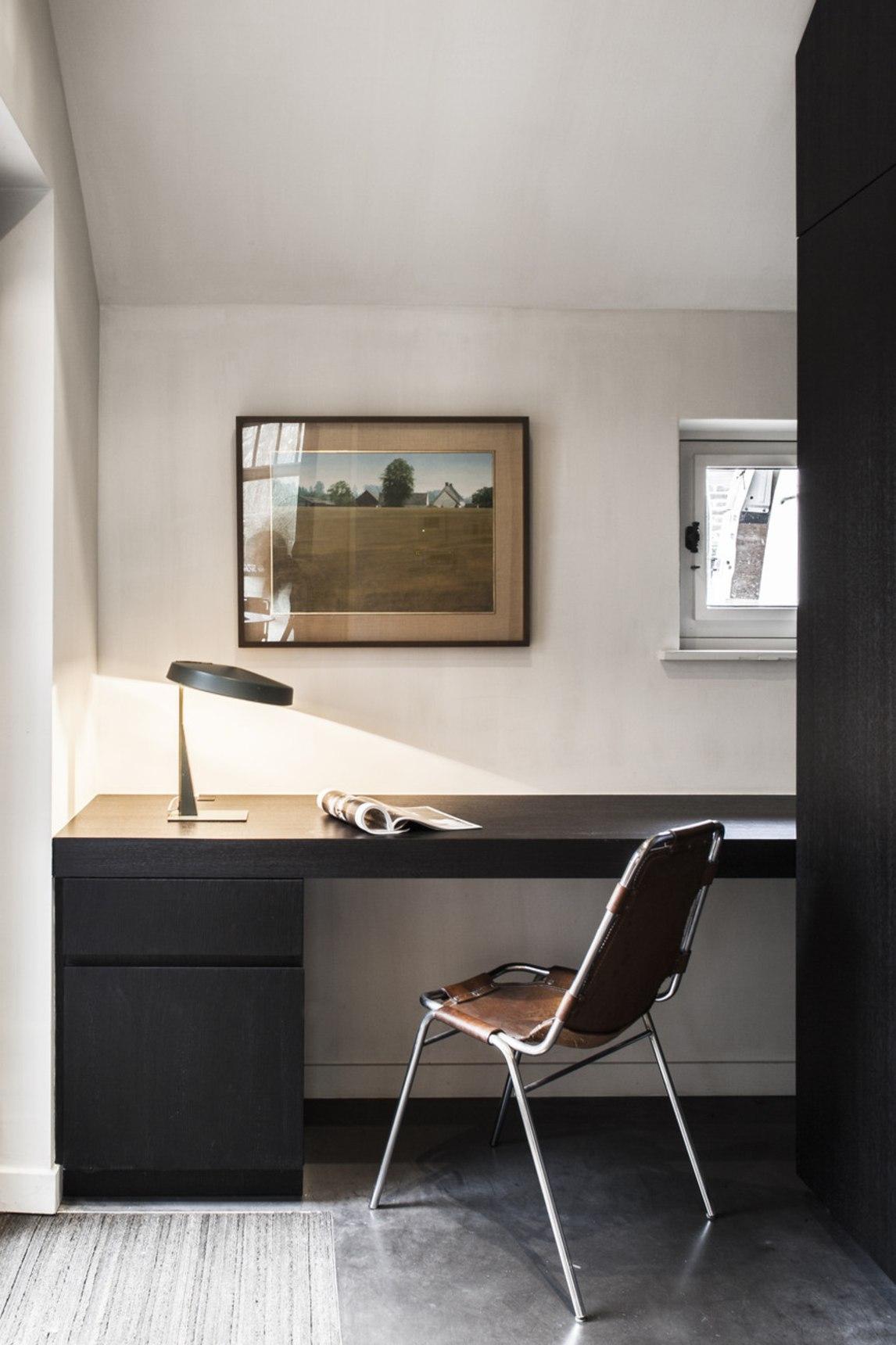 The workspace is very laconic, with dark furniture and a leather chair plus some art