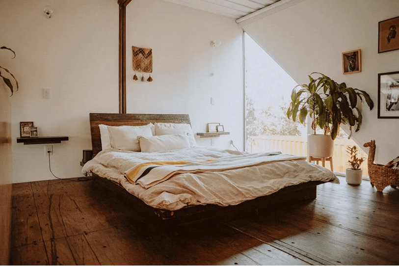 The bedroom is done with a triangle window, potted plants, a gallery wall and a stained bed with boho bedding