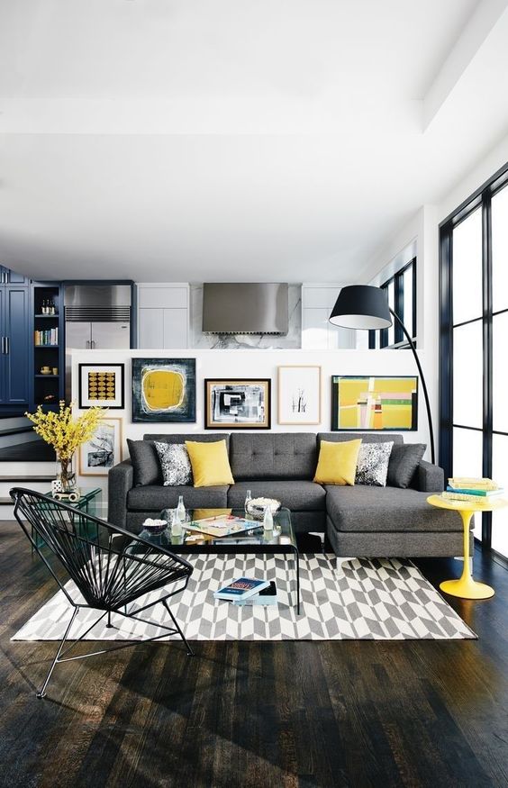 a bold living room with a grey corner sofa, with yellow pillows, a yellow table and a gallery wall in yellow, black and white is a statement space