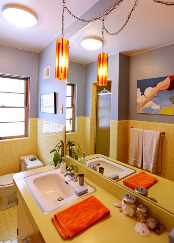 a bright bathroom with color block grey and yellow walls, with tiles and a yellow vanity, with a catchy pendant lamp